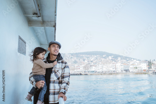 portrait of man carrying his daughter leaning against the railing of the ferryboat while crossing the sea