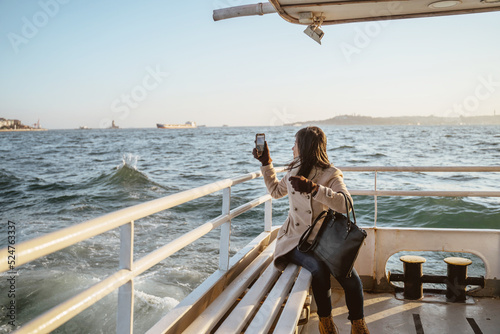 Valokuva woman sitting on a ferry boat crossing the bosphorus and taking photo using her