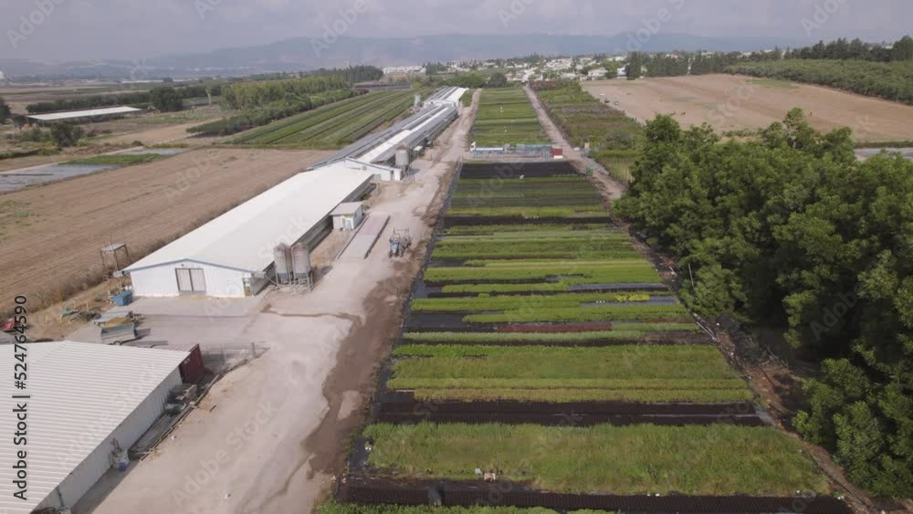 Aerial view of a tractor driving near fields of green plants in a kibbutz in northern Israel during the summer, mountains in the background, parallax to the right Aerial view of a tractor driving near fields of green plants in a kibbutz in northern Israel during the summer, mountains in the background, parallax to the right