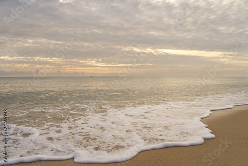 Morning sky with clouds from the beach. White surf on the sand with a small boat in the sea.