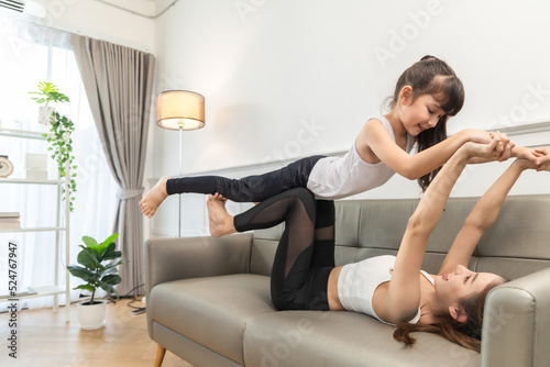 Asian young mother and her daughter setting prepare to yoga and meditation pose together on yoga mat in living room at home. Fitness lifestyle.