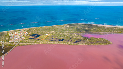 Areal photo of a Pink Lake right next to the blue ocean, separated by wild bushland.