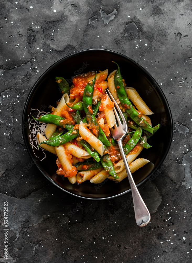 Vegetarian penne pasta with green beans and tomato sauce on a dark background, top view Vegetarian penne pasta with green beans and tomato sauce on a dark background, top view
