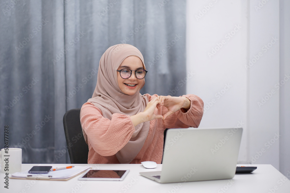 Beautiful asian muslim woman brown hijab making video call by digital laptop her hands making sign Heart by fingers. Beautiful asian muslim woman brown hijab making video call by digital laptop her hands making sign Heart by fingers.