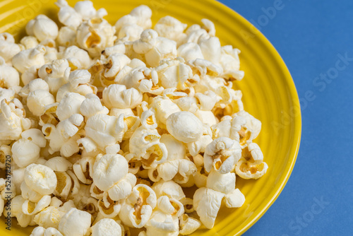 Popcorn on a yellow plate on blue background, Food or snack, Health or salt