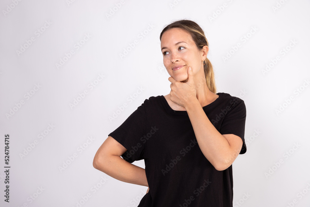 Portrait of pensive mid adult woman wearing black blouse. Thoughtful Caucasian woman standing with hand on chin over white background. Uncertainty and doubt concept