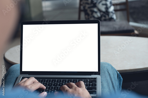 Mockup image of laptop computer. Casual business man, freelancer using and typing on laptop computer with blank white screen at coffee cup, over shoulder view