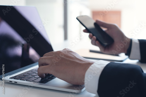 Businessman working on laptop computer and mobile phone with tablet on office table. Business man using smartphone, surfing the internet on laptop at workplace, close up