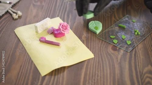 Stamping polymer clay leaf for flower. Artisan works with plastic in workshop. Craftsman uses silicone mold.
