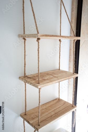 A view of a decorative wooden shelf held together by rope, mounted on the wall.