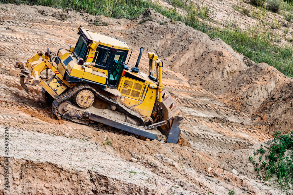 A powerful bulldozer in a sand pit is planning a site. Extraction of sand in an open pit. natural building materials.