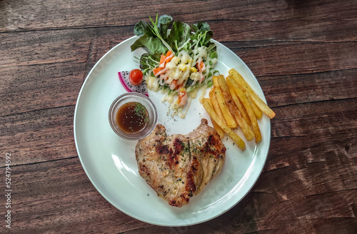 Fototapeta Naklejka Na Ścianę i Meble -  Pork Steak with French Fries, Sauce and Vegetable Salad on a white plate on a wooden table