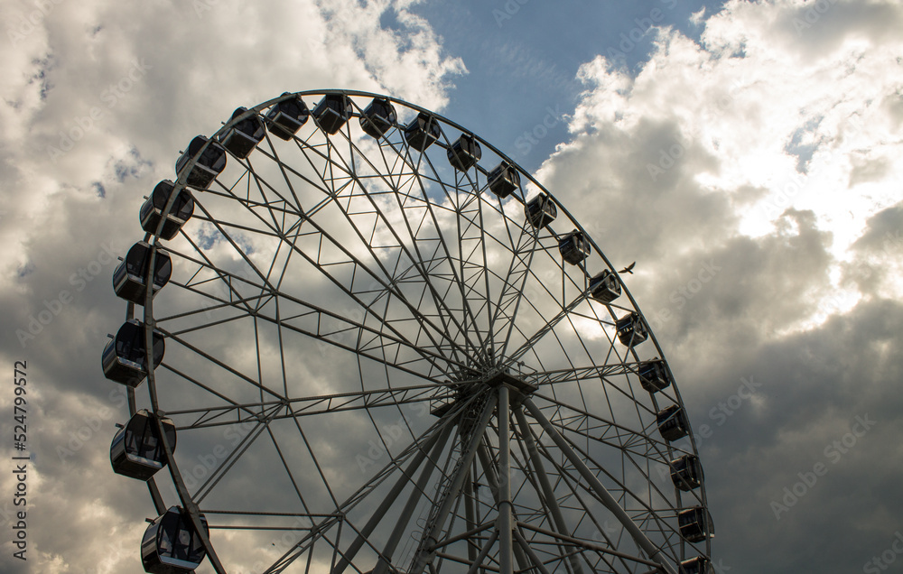 Vladimir, Russia - August, 16, 2022: Large metal Ferris wheel close-up against a blue sky with white clouds in town central park