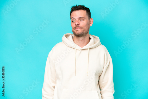 Young caucasian handsome man isolated on blue background having doubts while looking side