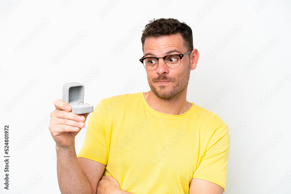 Young caucasian man holding a engagement ring isolated on white background with sad expression Young caucasian man holding a engagement ring isolated on white background with sad expression
