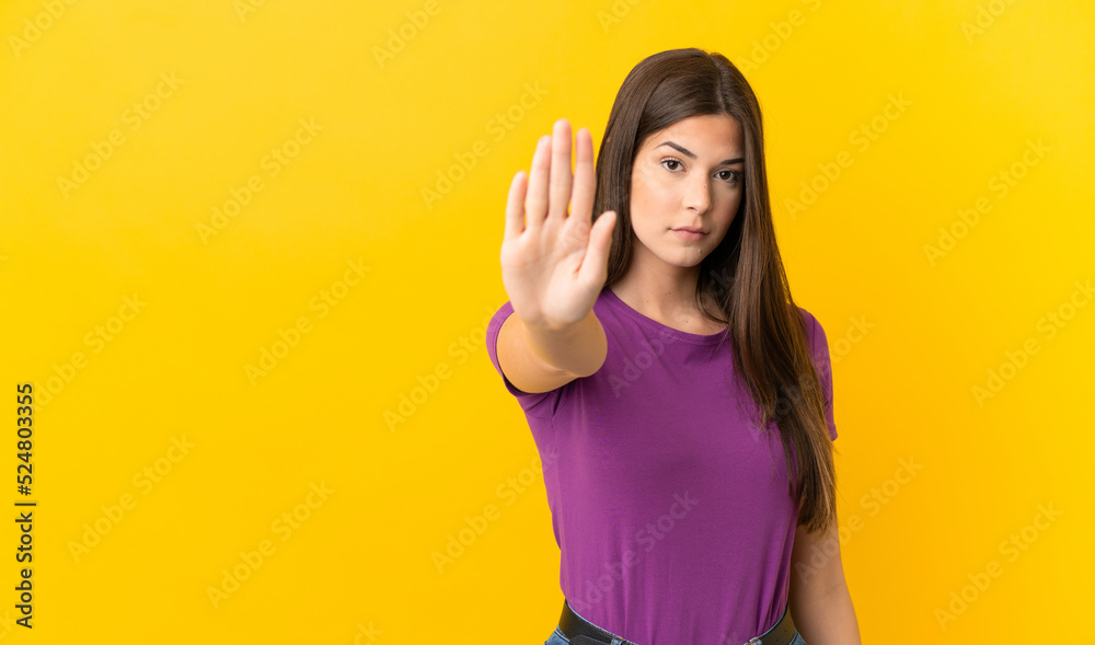 Teenager Brazilian girl over isolated yellow background making stop gesture Teenager Brazilian girl over isolated yellow background making stop gesture