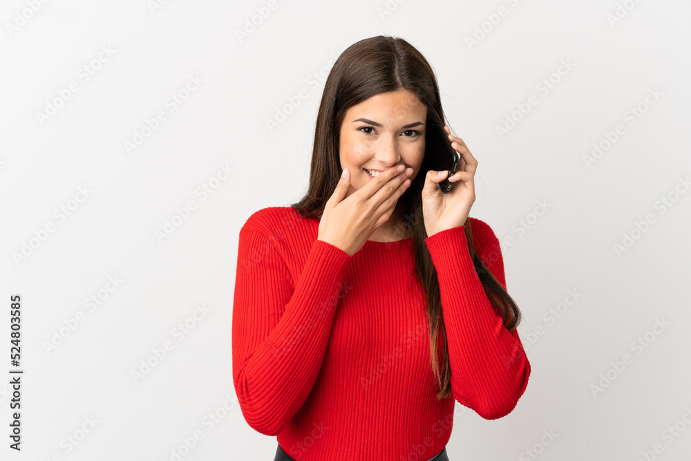 Teenager Brazilian girl using mobile phone over isolated white background happy and smiling covering mouth with hand Teenager Brazilian girl using mobile phone over isolated white background happy and smiling covering mouth with hand