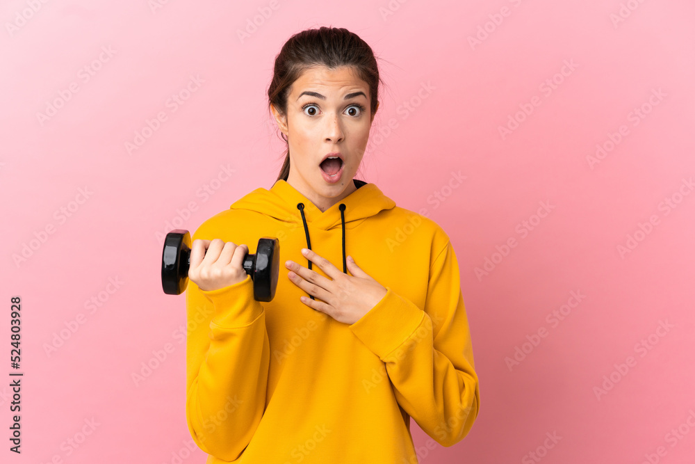 Young sport girl making weightlifting over isolated pink background surprised and shocked while looking right Young sport girl making weightlifting over isolated pink background surprised and shocked while looking right