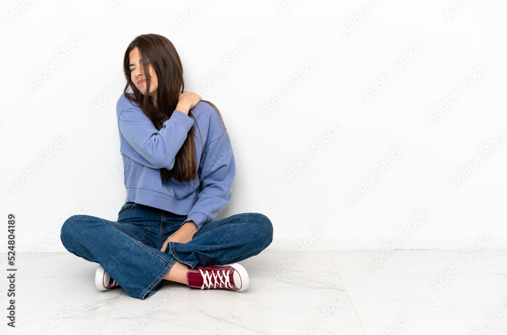 Young woman sitting on the floor suffering from pain in shoulder for having made an effort Young woman sitting on the floor suffering from pain in shoulder for having made an effort