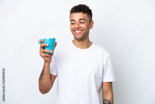 Young Brazilian man holding cup of coffee isolated on white background with happy expression © luismolinero