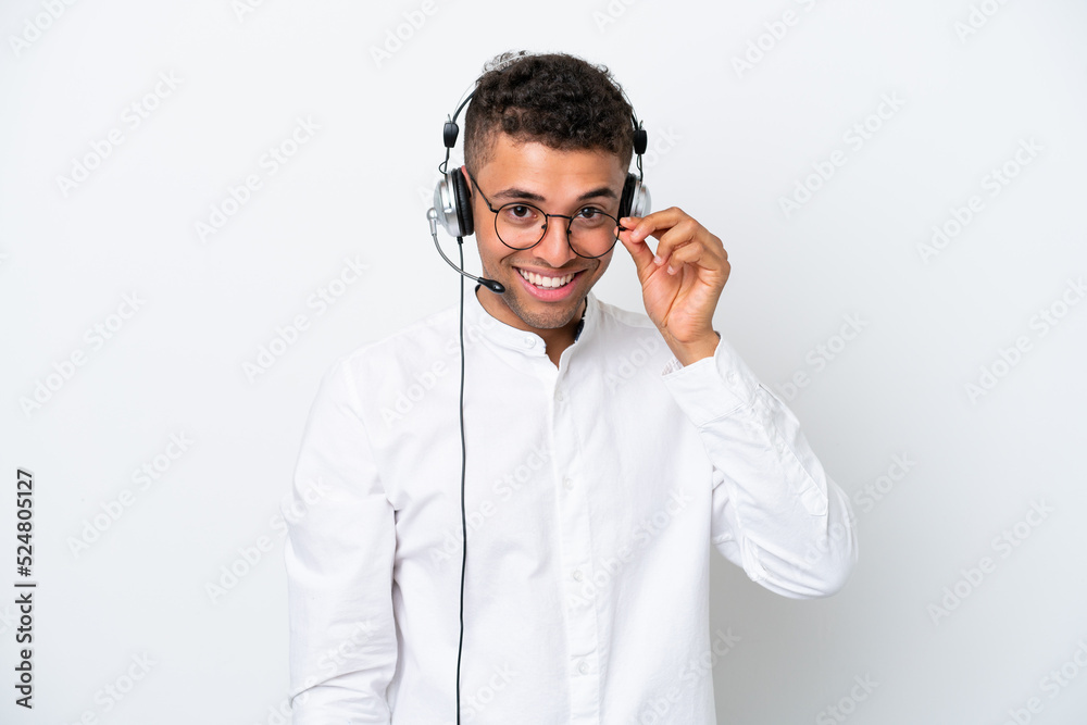 Telemarketer Brazilian man working with a headset isolated on white background with glasses and happy Telemarketer Brazilian man working with a headset isolated on white background with glasses and happy