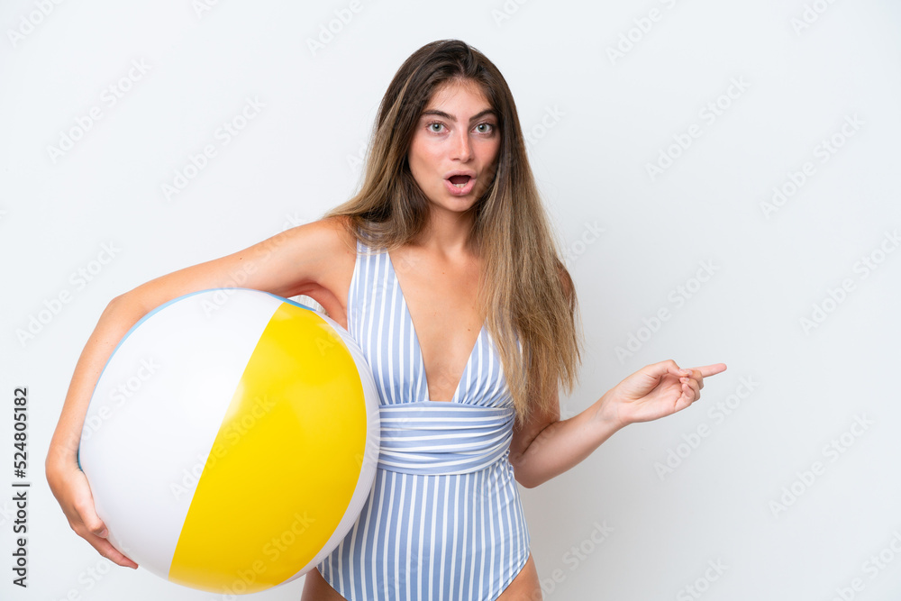 Young woman in swimsuit holding beach ball isolated on white background surprised and pointing side Young woman in swimsuit holding beach ball isolated on white background surprised and pointing side