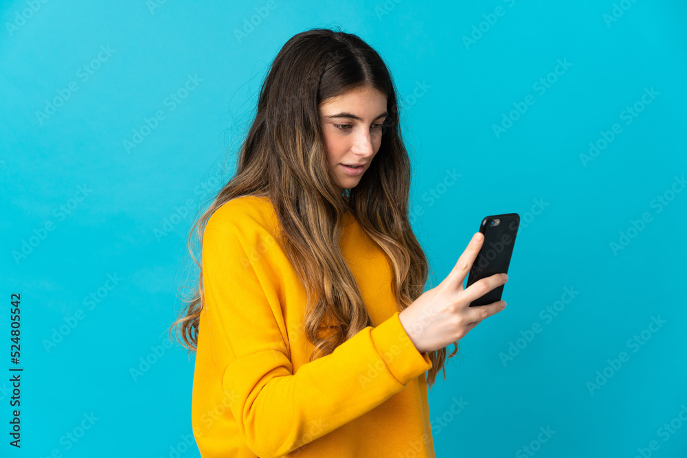Young caucasian woman isolated on blue background sending a message or email with the mobile Young caucasian woman isolated on blue background sending a message or email with the mobile
