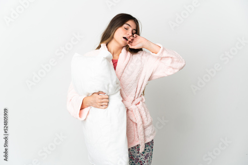Young caucasian woman isolated on white background in pajamas and holding a pillow and yawning