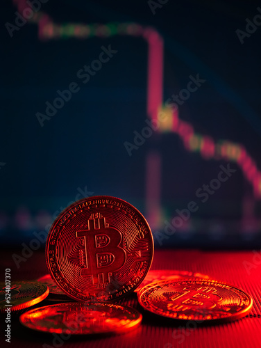 Coins with bitcoin symbol on red light and crypto stocks chart background. Concept of a cryptocurrency market crisis.