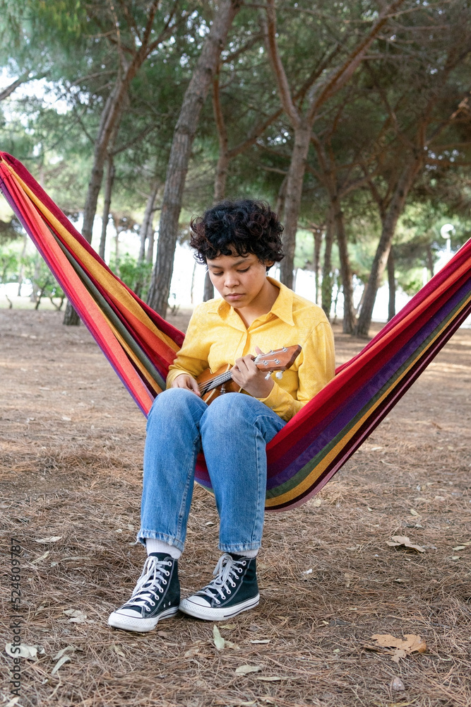 Cheerful woman playing ukulele sitting in hammock Cheerful woman playing ukulele sitting in hammock