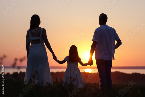 Happy family runs towards sun joining hands to look at picturesque landscape. Daughter leads father and mother running on meadow to look at first sunset in life
