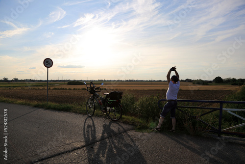 Mężczyzna z podniesionymi rękoma i rowerem turystycznym na tle zachodzącego słońca.