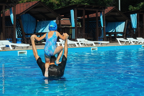 Individual swimming lessons with children in the outdoor pool during the warm season. The coach teaches a sports girl to keep balance and dive into the water of the pool from his shoulders correctly