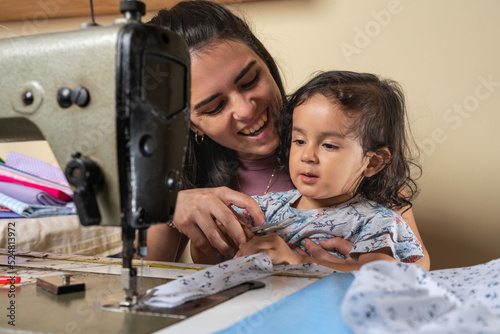 Positive Hispanic mother with girl at sewing machine photo