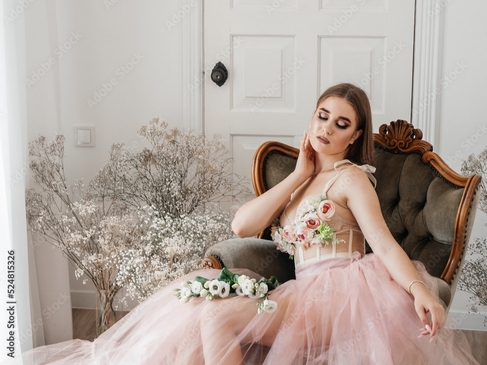 A girl with voluminous hair poses in a pink dress with flowers in her hands