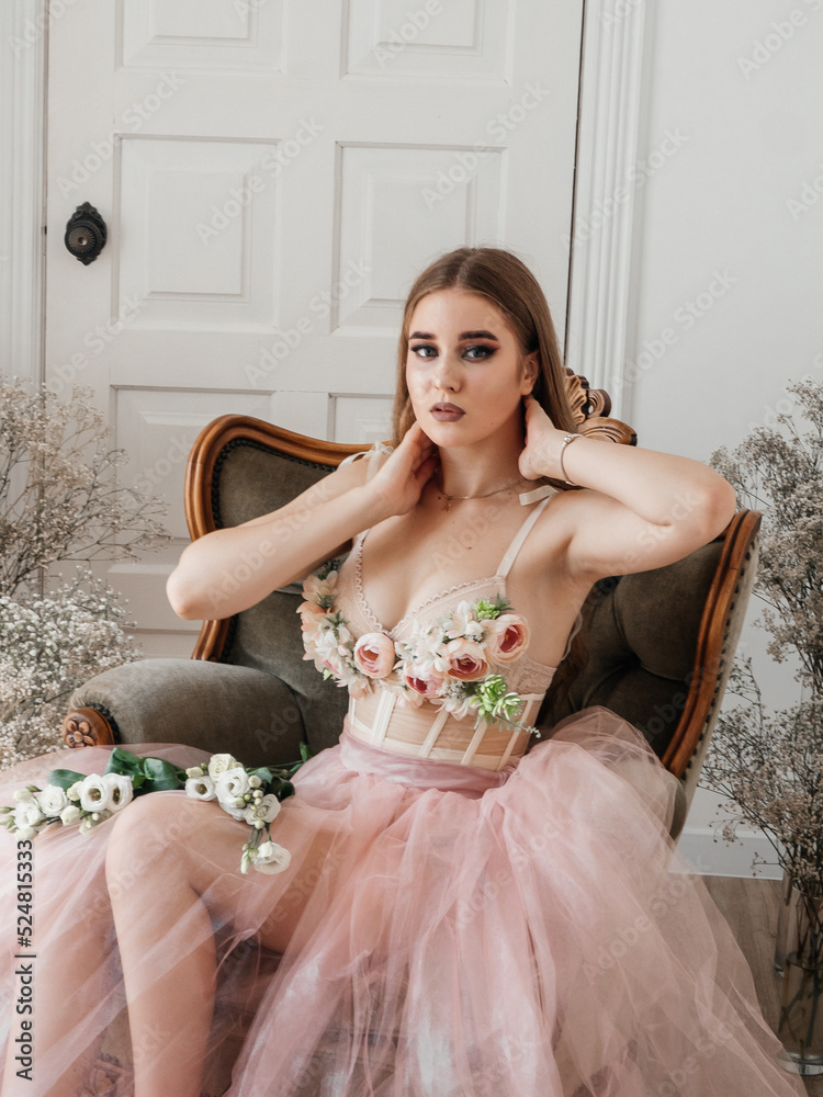 A girl with voluminous hair poses in a pink dress with flowers in her hands