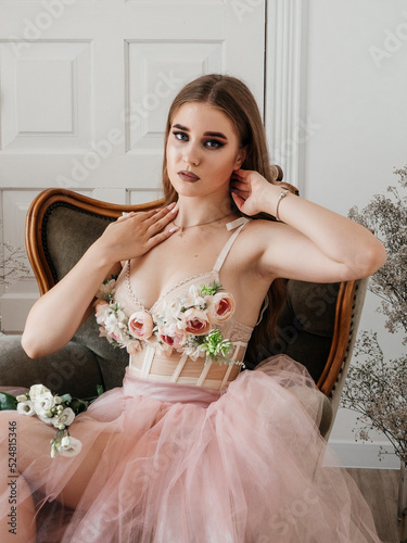 A girl with voluminous hair poses in a pink dress with flowers in her hands