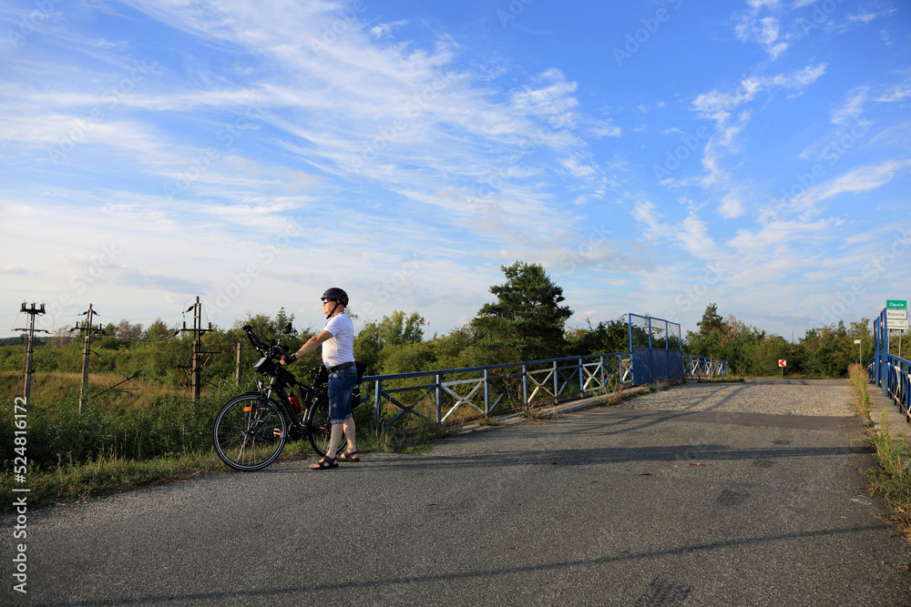 Mężczyzna z rowerem turystycznym na tle wiaduktu kolejowego. - obrazy, fototapety, plakaty 