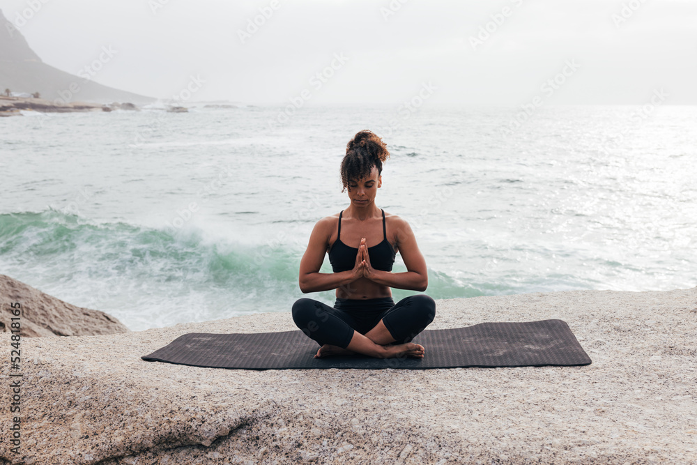 Fit woman with crossed legs meditating while sitting on mat by ocean