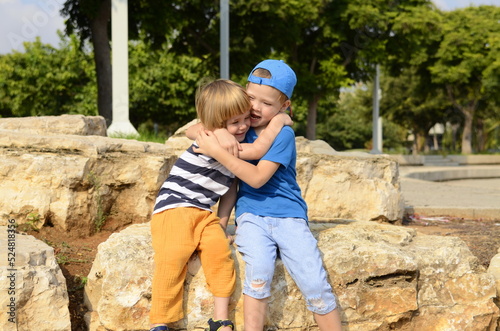 Two little boys, two friends, brothers are sitting on the street embracing. Concept: friendship, family, adventure, childhood, preschool education, kindergarten, amusement park, traveling with childre