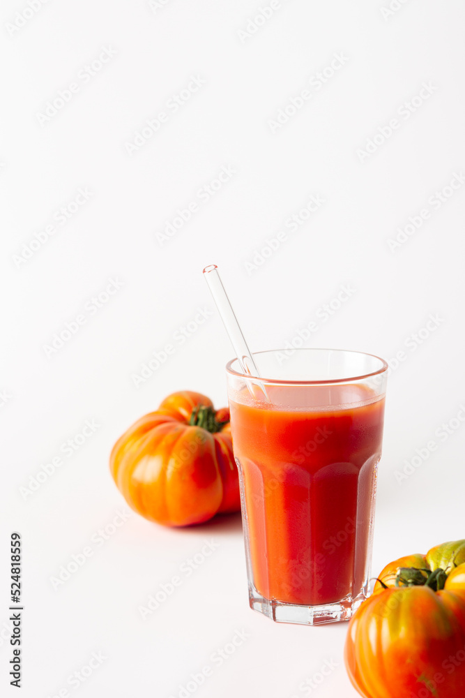 Homemade freshly squeezed tomato juice in a glass with a glass straw and tomatoes on a white background Homemade freshly squeezed tomato juice in a glass with a glass straw and tomatoes on a white background