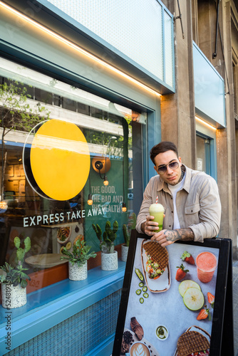 Tattooed man with takeaway glass of smoothie on city street photo