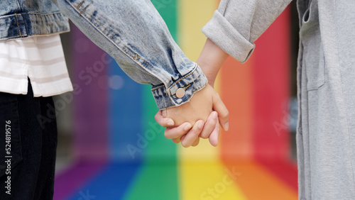 Closeup young adult queer transgender lover asia two people hold hand with colorful stripes flag. Proud of LGBT or LGBTQIA partner culture hug love sign in bisexual festival march day at city street.