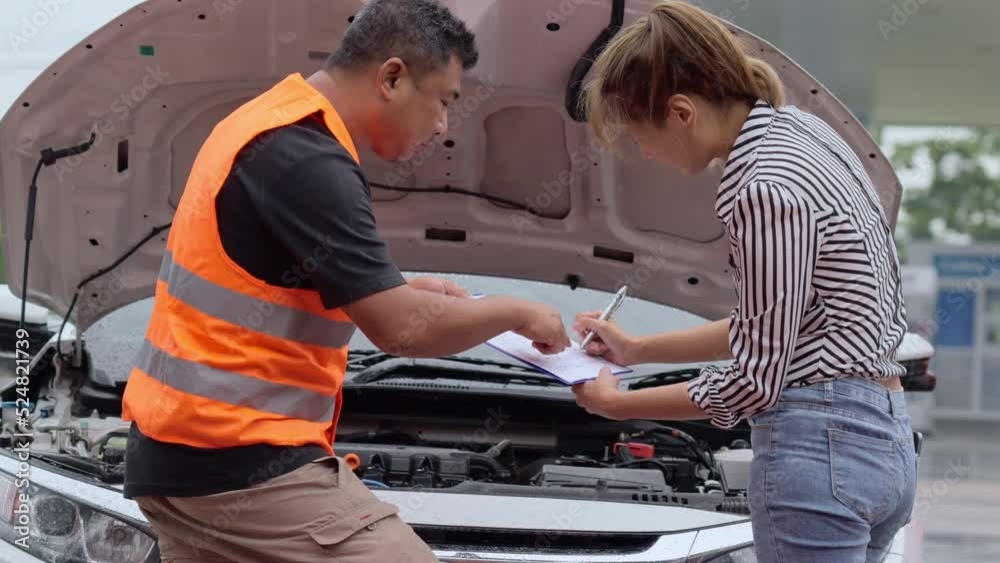 Worried young Asian woman talking to a car insurance agent or technician to claim the repair on her car accident and signing the claim form Worried young Asian woman talking to a car insurance agent or technician to claim the repair on her car accident and signing the claim form