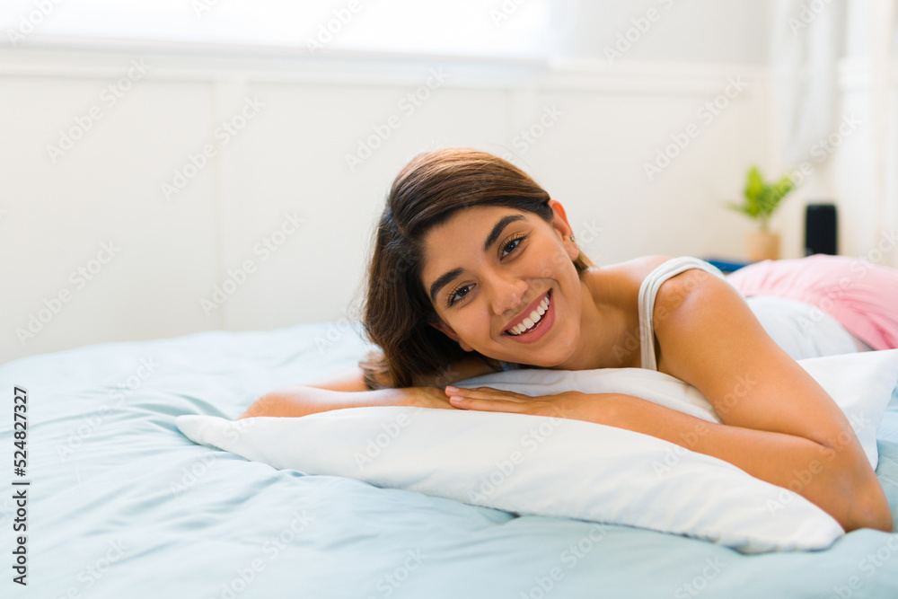 Beautiful woman looking happy while lying on her stomach in bed