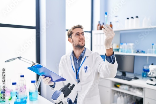 Young man scientist reading report holding test tube at laboratory