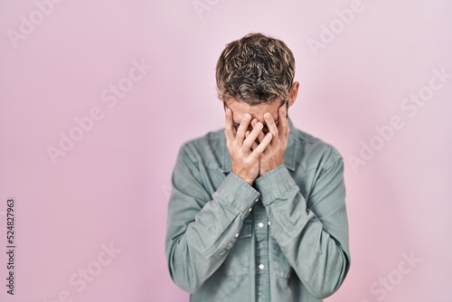 Hispanic man with beard standing over pink background with sad expression covering face with hands while crying. depression concept.