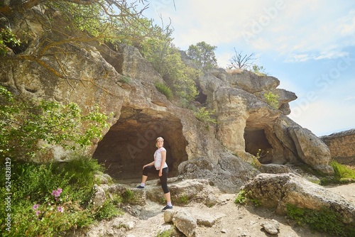 A school-age girl near the entrance to a cave in a rock. The concept of tourism.