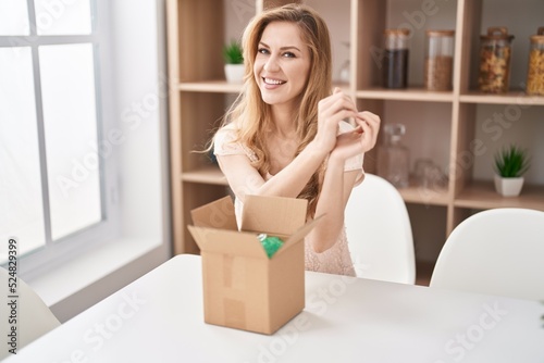 Beautiful blonde woman with cardboard box smiling in love doing heart symbol shape with hands. romantic concept.