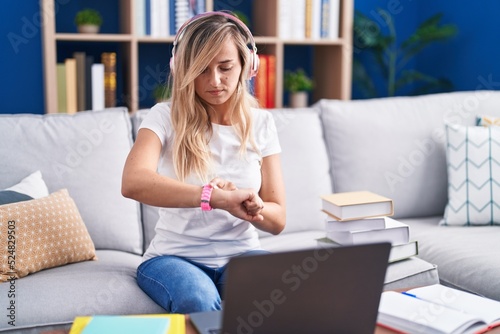 Young blonde woman studying using computer laptop at home checking the time on wrist watch, relaxed and confident